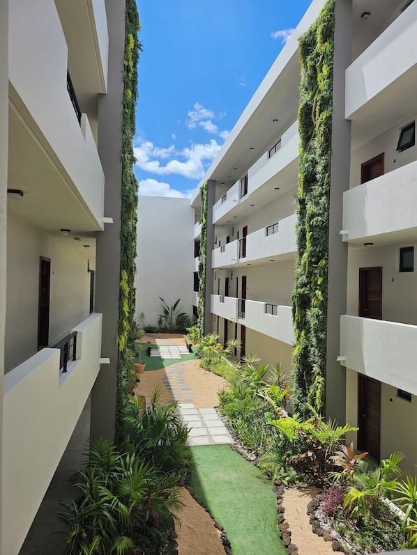 A modern building with a central courtyard featuring a paved walkway, surrounded by lush greenery and white walls.
