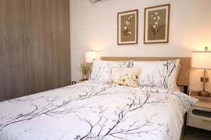 Ein Schlafzimmer mit einem Bett, zwei an der Wand befestigten Blumenbildern, einem Nachttisch mit Lampe und einem Kleiderschrank.