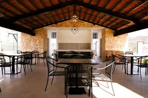 Un espace extérieur aménagé pour les repas, avec des murs en pierre, une table centrale et des chaises.