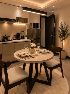 Una cocina moderna con comedor, que incluye una mesa redonda dispuesta para dos personas, una cafetera y un refrigerador.
