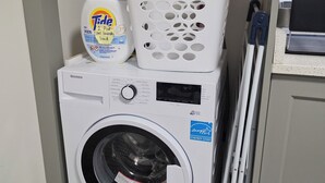 Eine Waschmaschine mit Frontlader, ein Bedienelement, ein weißer Wäschekorb und ein Waschmittelbehälter.