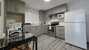 Eine moderne Küche mit grauen Schränken, einem Edelstahlbackofen, einem weißen Kühlschrank und einem Essbereich mit einem Glastisch.