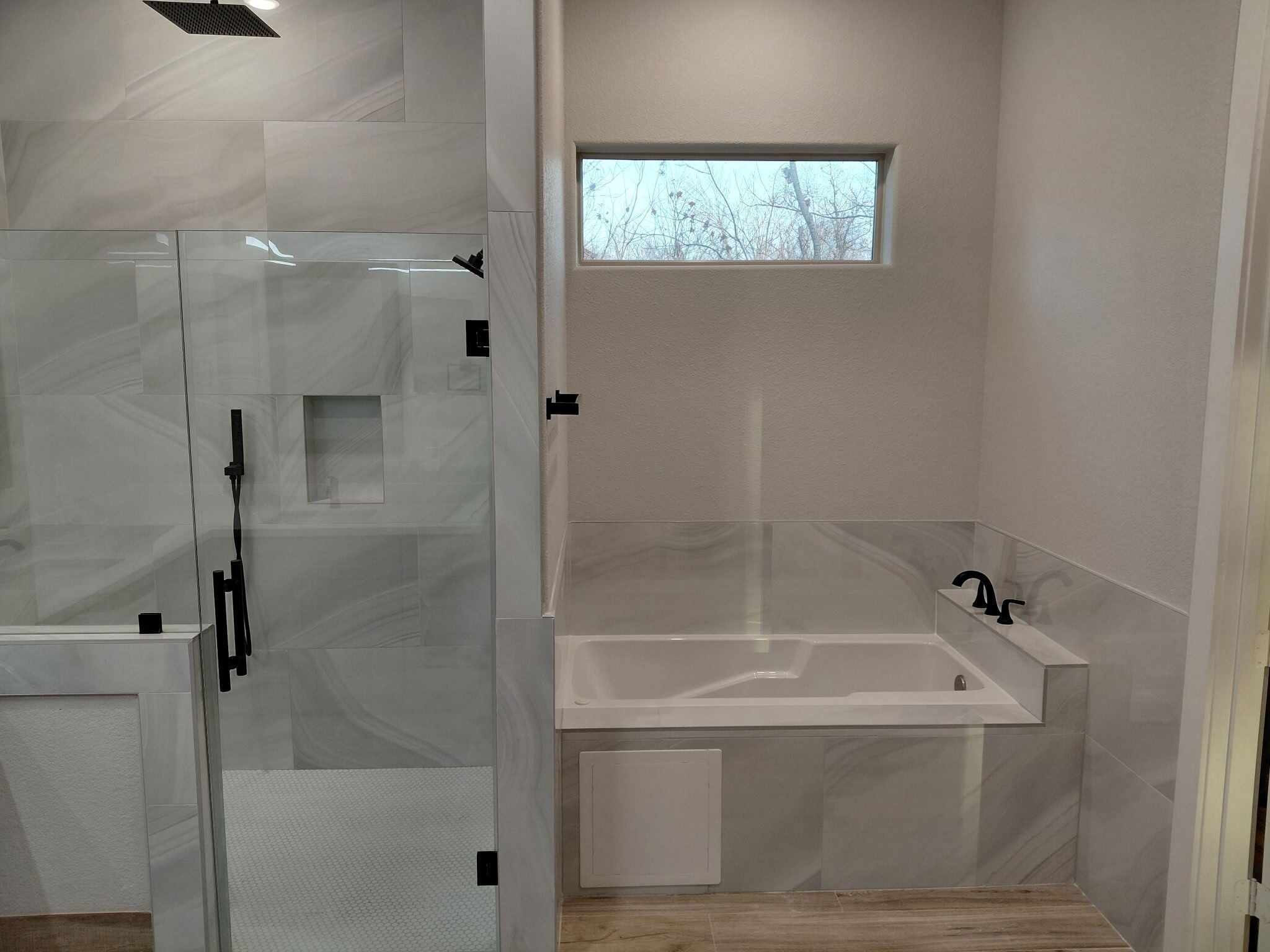 A modern bathroom with a glass shower enclosure, a bathtub, and a small window.