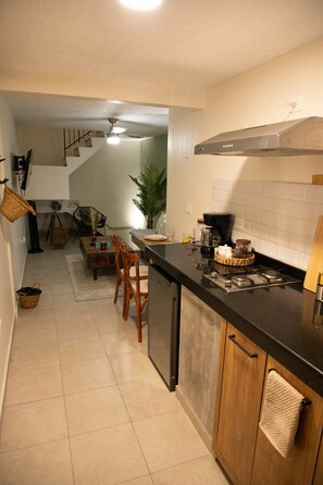 A kitchen with a black countertop, wooden cabinets, a stove, and a dining area with chairs and a table.