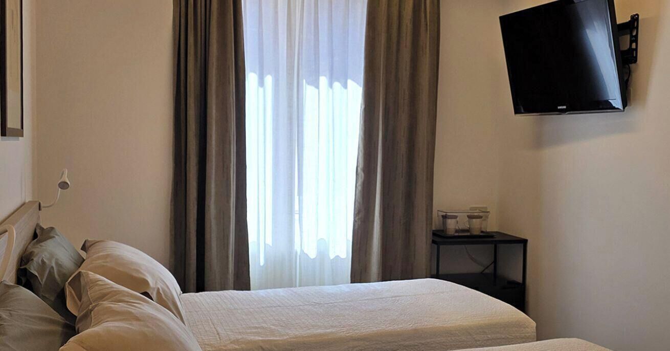 Een hotelkamer met een bed, gordijnen, een aan de muur bevestigde televisie en een klein tafeltje met spullen erop.