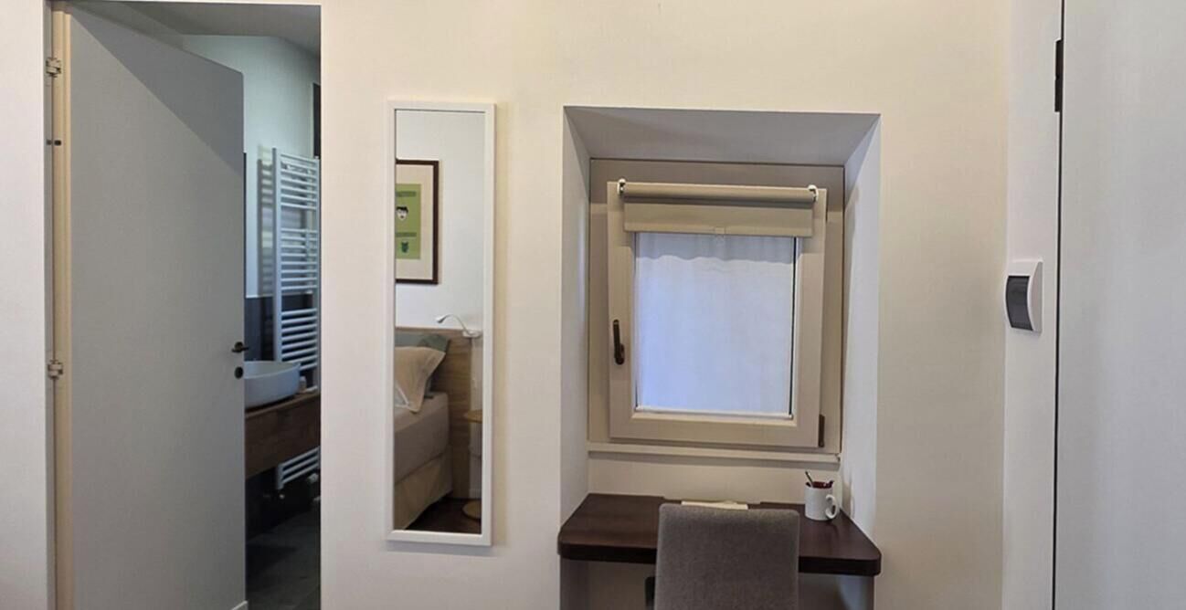 Ein kleines Zimmer mit Fenster, Spiegel, Handtuch und Schreibtisch.