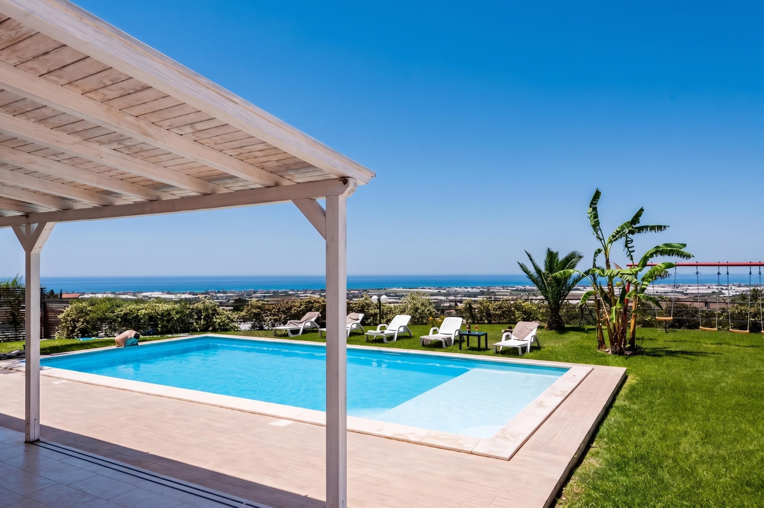 A pool area with a view of the ocean and a clear sky.