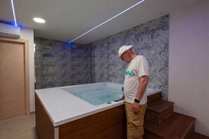 A man standing by a large bathtub in a room with a wooden floor and a patterned wall. - Villa Giardino Sul Mare - Scicli (Scicli)