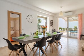 A modern dining area with a table set for four, a clock on the wall, and a view of the outdoors. - Villa Giardino Sul Mare - Scicli (Scicli)