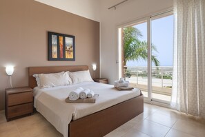 A bedroom with a bed, nightstands, a painting, and a view of the outdoors.