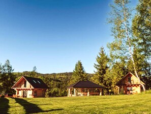 Une cabane rustique dotĂ©e dâune grande vĂ©randa, une cabane plus petite avec une vĂ©randa couverte, et une structure en bois situĂ©e dans un champ herbeux.