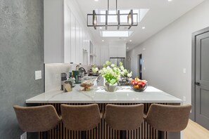A modern kitchen with a central island, pendant lighting, and a view to the dining area. - Entire Boston Home / New Build (Somerville)