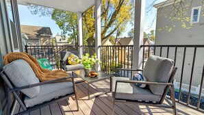 Une terrasse extérieure couverte, avec deux fauteuils gris rembourrés, une petite table agrémentée d’une plante et un logo jaune et noir sur le mur.