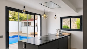 A modern kitchen with a large island, a built-in dishwasher, and a window overlooking a pool. - Villa Avril · 7 bedrooms, large pool, and unique terraces near Sitges (Olivella)
