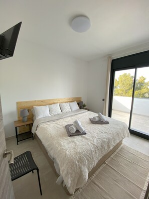 A bedroom with a large bed, a wooden headboard, a nightstand with a lamp, and a view of the outdoors through a sliding door.