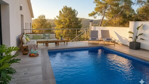 A swimming pool with a wooden deck, lounge chairs, and a view of trees and hills. - Villa Avril · 7 bedrooms, large pool, and unique terraces near Sitges (Olivella)