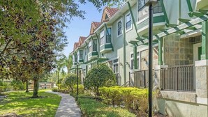Fileira de casas urbanas com detalhes verdes, um caminho pavimentado e paisagismo bem cuidado.