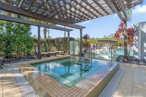 Ein Poolbereich mit Pergola, Liegestühlen und einem kleinen Wasserfall.