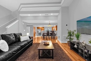 Ein modernes Wohnzimmer mit einem schwarzen Ledersofa, einem Holztisch und einem Essbereich im Hintergrund.