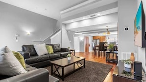 A modern living room with a sofa, coffee table, and a TV. There is a staircase leading to another room.