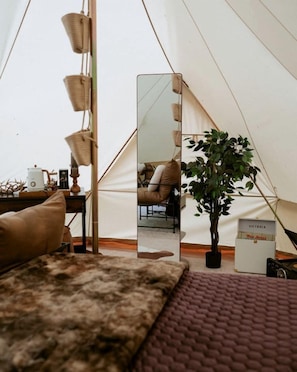 A tent interior with a bed, a mirror, a potted plant, a table with a lamp, and a box labeled 'VICTORIA.' - Private Luxury Glamping Tent with Delaware River Access Near Long Eddy, NY (Long Eddy)