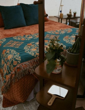 Una cama con colcha floral, una pequeña planta en maceta y un espejo con marco de madera.