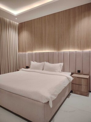 A modern bedroom with a large bed, a wooden headboard, and a nightstand. - Rama Dubai Serviced Apartments Hafsa (Riyadh)
