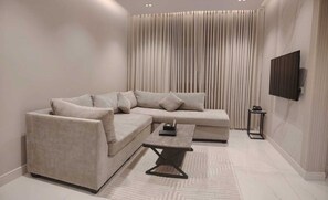 Uma sala de estar moderna com um sofá seccional, uma mesa de centro e uma TV na parede.