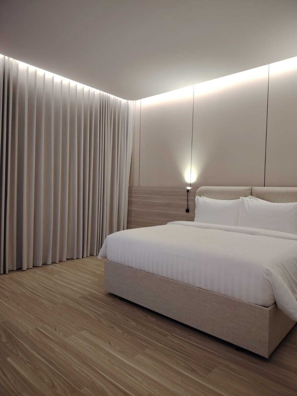 A modern bedroom with a large bed, wooden flooring, and a wall-mounted light fixture.