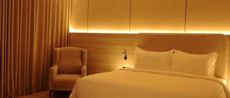 A modern hotel room with a large bed, a seating area, and a wall-mounted light fixture.