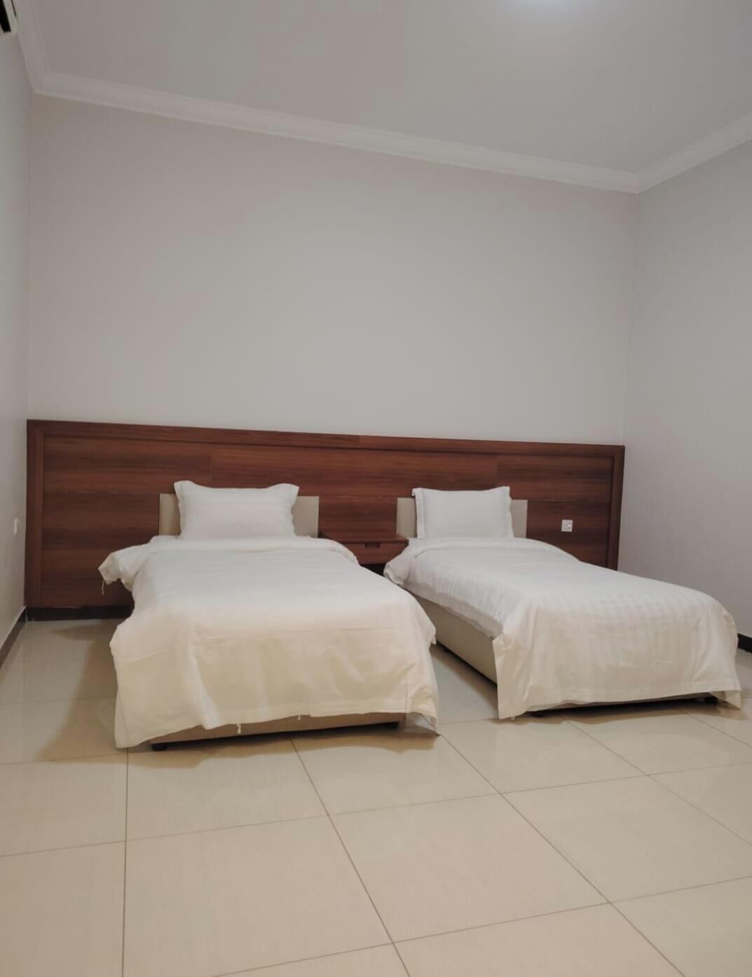 A room with two single beds, a wooden headboard, and a tiled floor.
