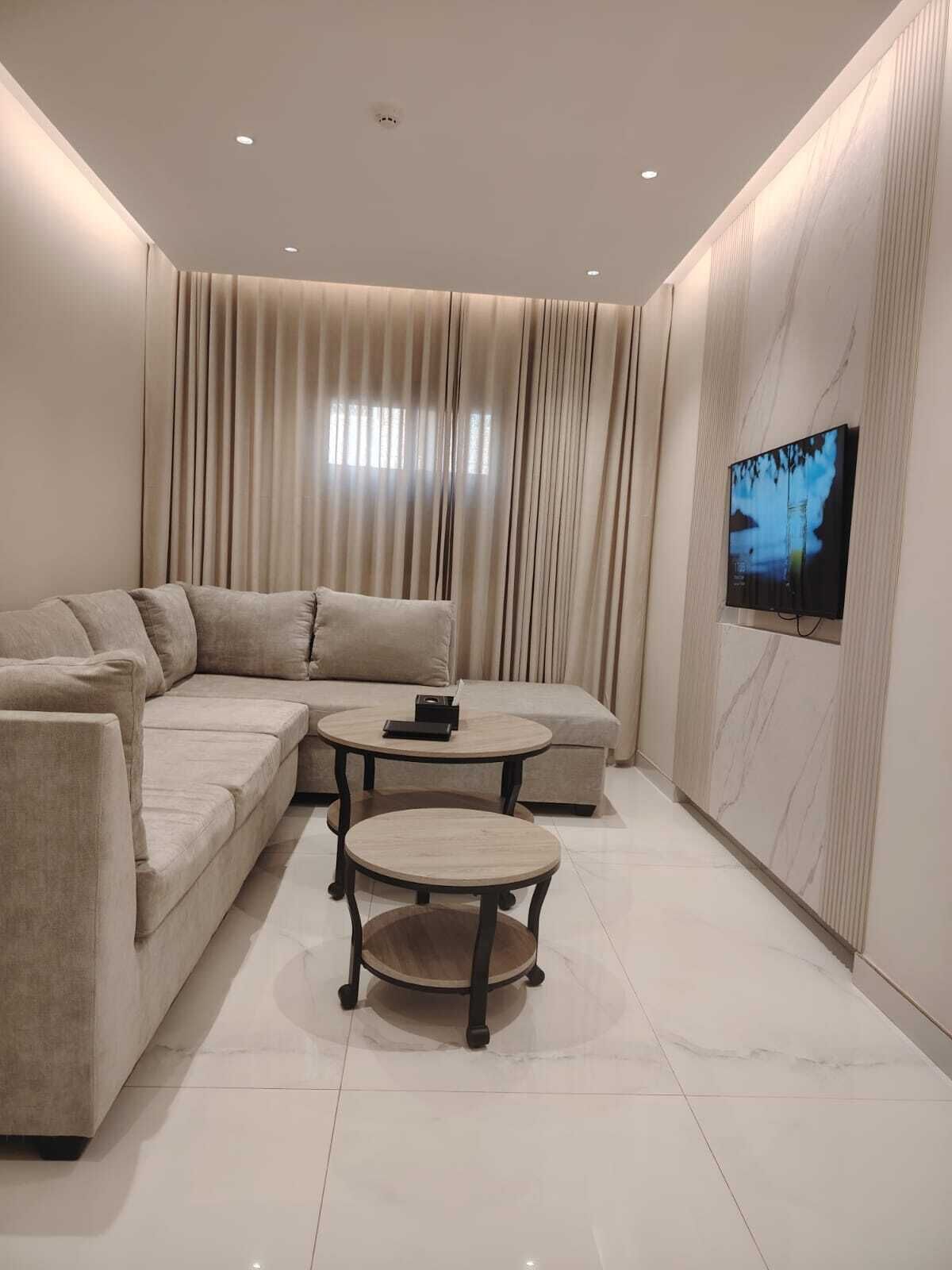 Un salon moderne avec un canapé d’angle, une table basse ronde et un téléviseur à écran plat fixé au mur.