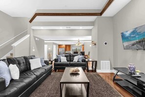 Ein modernes Wohnzimmer mit einem schwarzen Ledersofa, einem Holztisch und einem flachbildfernseher an der Wand.