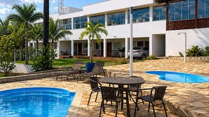 A modern building with a swimming pool, outdoor seating, and palm trees.