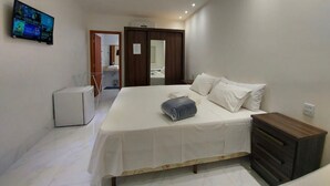 A bedroom with a bed, a dresser, a TV, and a small refrigerator.