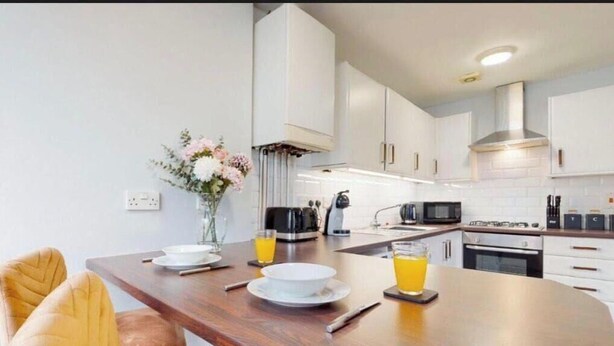 A modern kitchen with white cabinets, a wooden dining table, and a vase with flowers. - Affordable Luxury At The Heart Of The City (Cardiff)