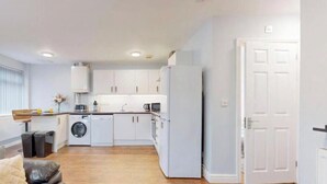 A compact living space with a kitchenette, a washing machine, a sofa, and a door. - Affordable Luxury At The Heart Of The City (Cardiff)