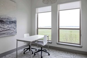 Ein Zimmer mit weißem Tisch und Stühlen, großen Fenstern mit Blick auf ein Feld und einem modernen, abstrakten Gemälde an der Wand.