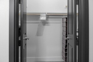 Un dressing ouvert avec une tringle en bois et des étagères, une porte avec un cadre noir et un mur blanc.