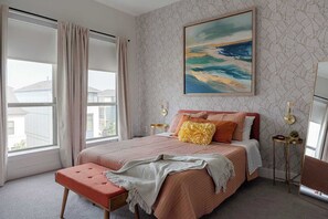 Ein Schlafzimmer mit einem großen Bett, einer Bank, einem Nachttisch, einer Uhr und einem Fenster mit Vorhängen.