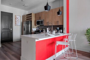 Une cuisine moderne dotée d’un îlot central, d’appareils électroménagers en acier inoxydable et d’un mur d’accent rouge.