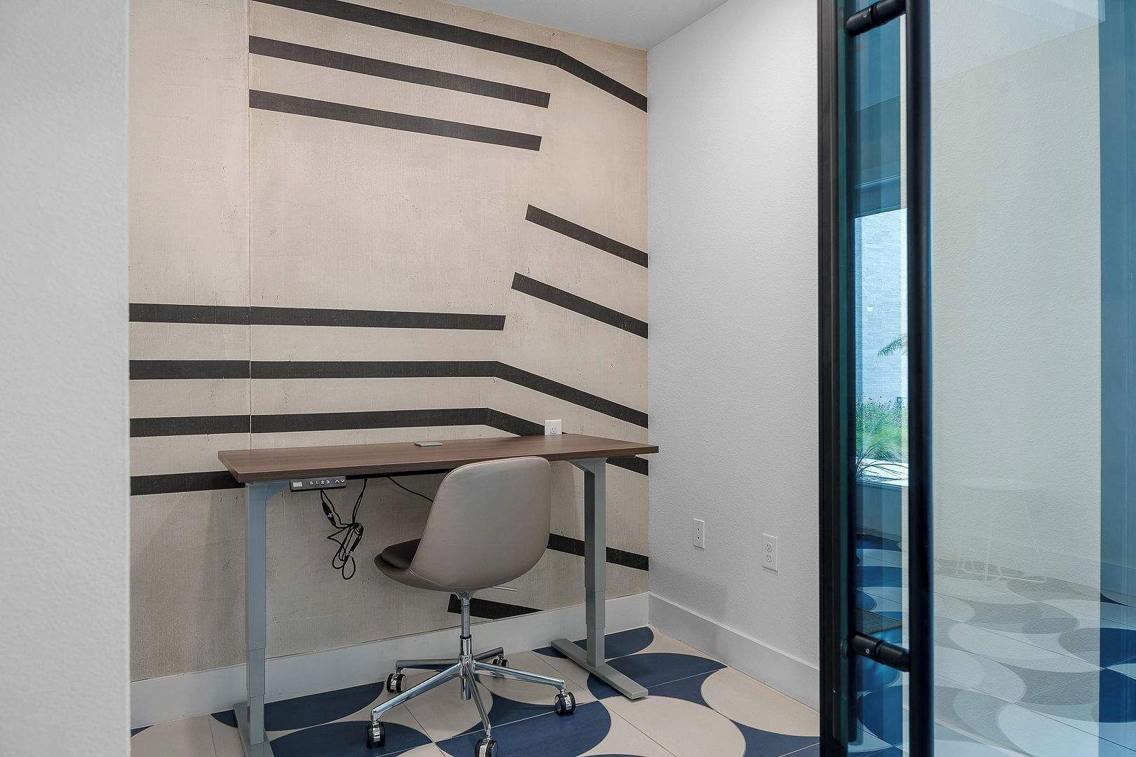 Un espace de bureau moderne avec un bureau, une chaise et un mur orné d’un motif.