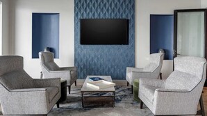 Uma sala de estar moderna com televisão de tela plana, dois poltronas, uma mesa de centro e um papel de parede estampado.