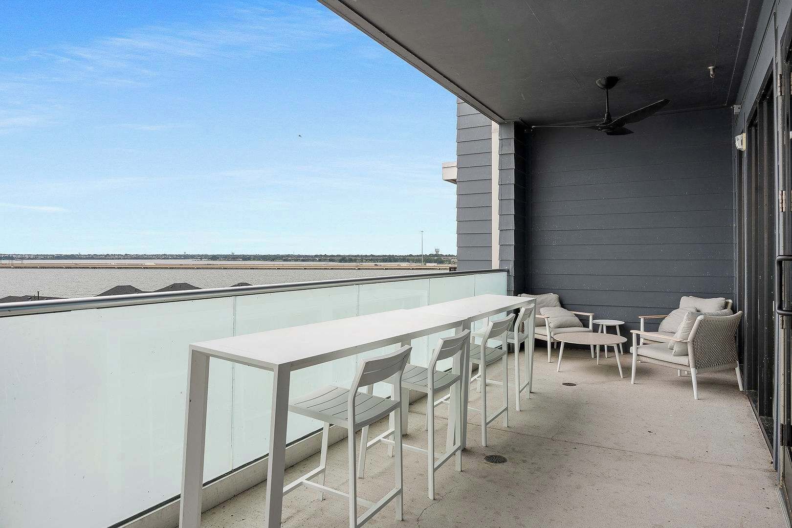 Un balcon avec une table et des chaises blanches, un ventilateur de plafond et une vue sur la plage.