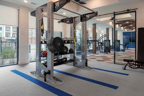 Ein Fitnessraum mit Krafttrainingsgeräten, einer blauen Matte und Blick auf Gebäude im Freien.