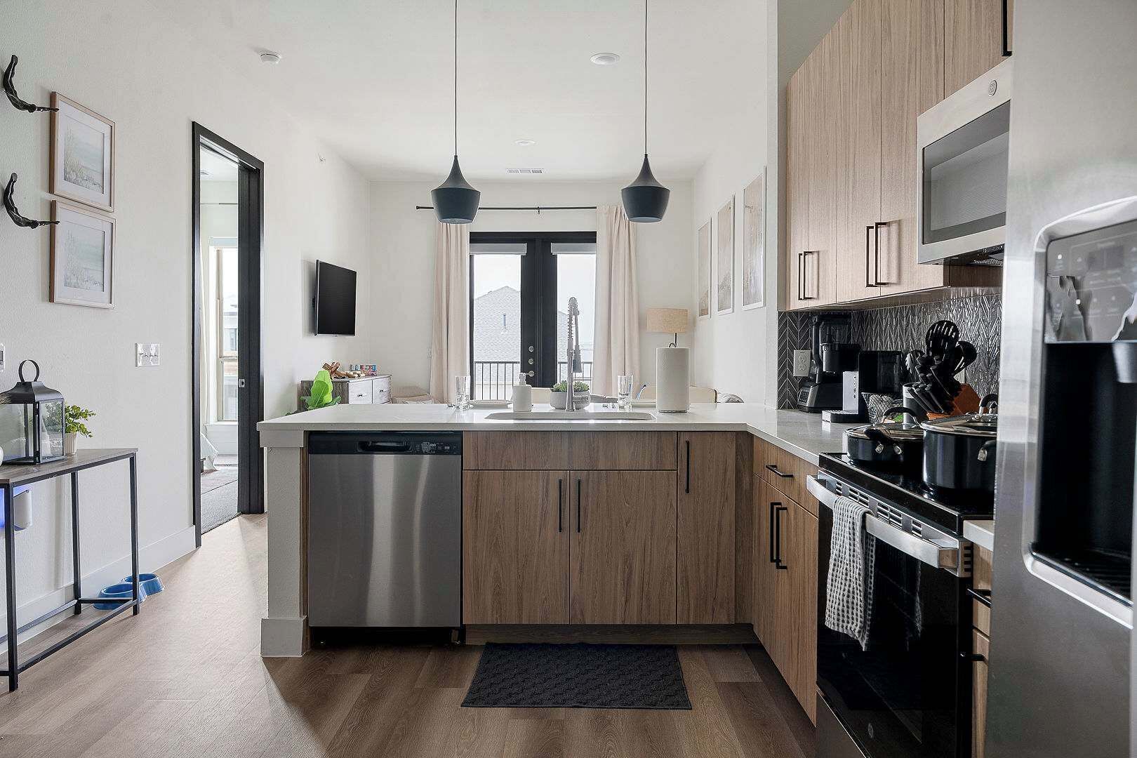 A modern kitchen with wooden cabinets, stainless steel appliances, and pendant lighting.