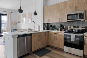 A modern kitchen with stainless steel appliances, wooden cabinets, and a dishwasher. - Sapphire Shores | Lakeside Escape, Pet Friendly (Rowlett)