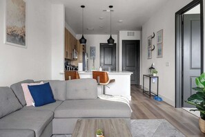 A modern living room with a grey sofa, a coffee table, and a kitchen in the background. - Sapphire Shores | Lakeside Escape, Pet Friendly (Rowlett)