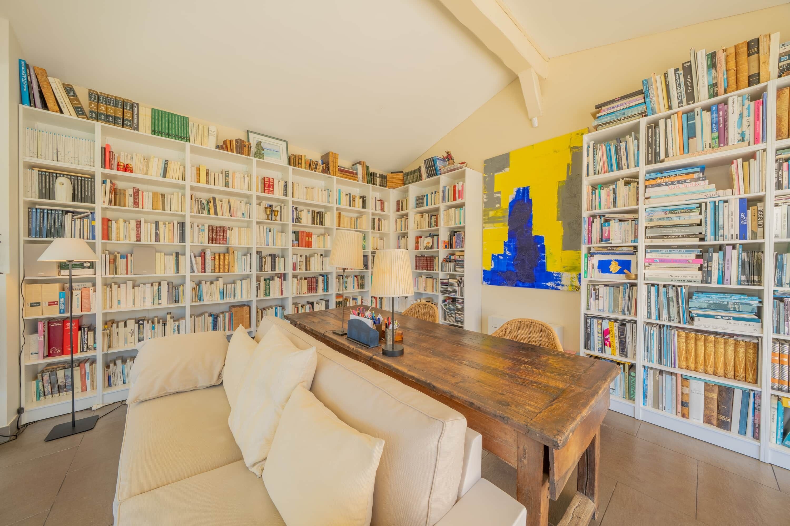 A library with bookshelves, a wooden table, and a sofa.