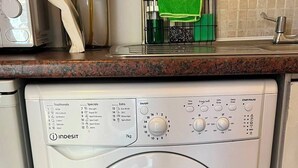 Un lave-linge à chargement frontal doté d’un panneau de commande, un plan de travail de cuisine avec un four à micro-ondes et un tapis à rayures.